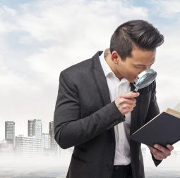 young asian business man looking through a magnifying glass