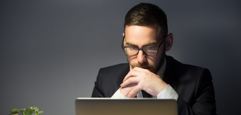 Concerned worker looking at laptop screen, thinking about problem solution, risks, company success strategies, person reading financial report. Concept of hardworking, concentration, making decision